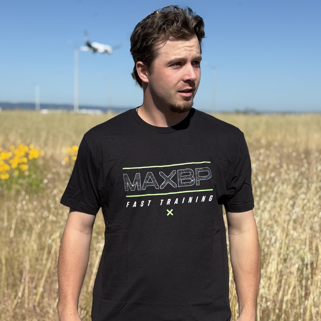 Man wearing a black t-shirt with 'MAXBP' logo in a field