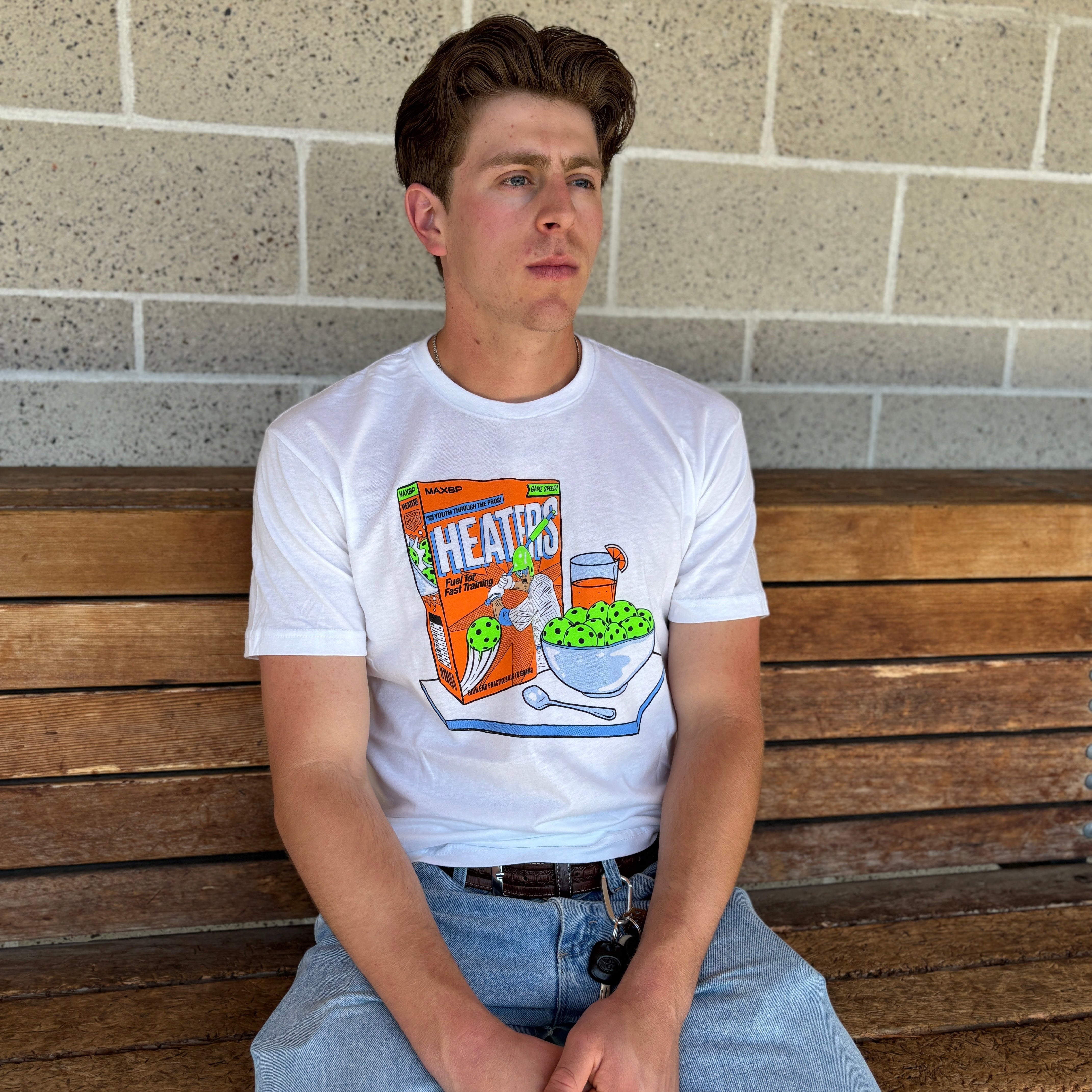 Person wearing a white t-shirt with a graphic design sitting on a wooden bench against a brick wall.