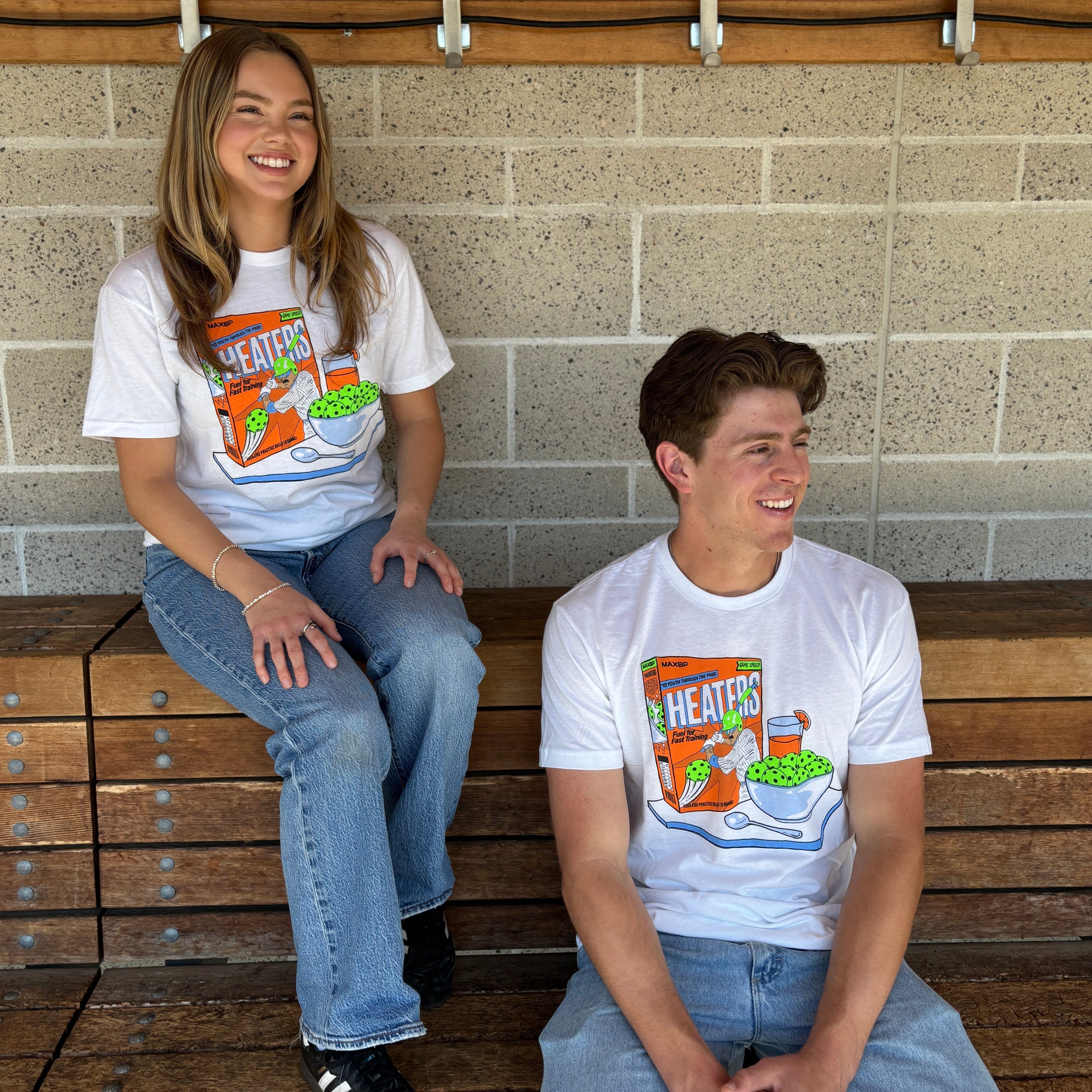 Two people sitting on wooden benches wearing matching t-shirts with a cartoon design.