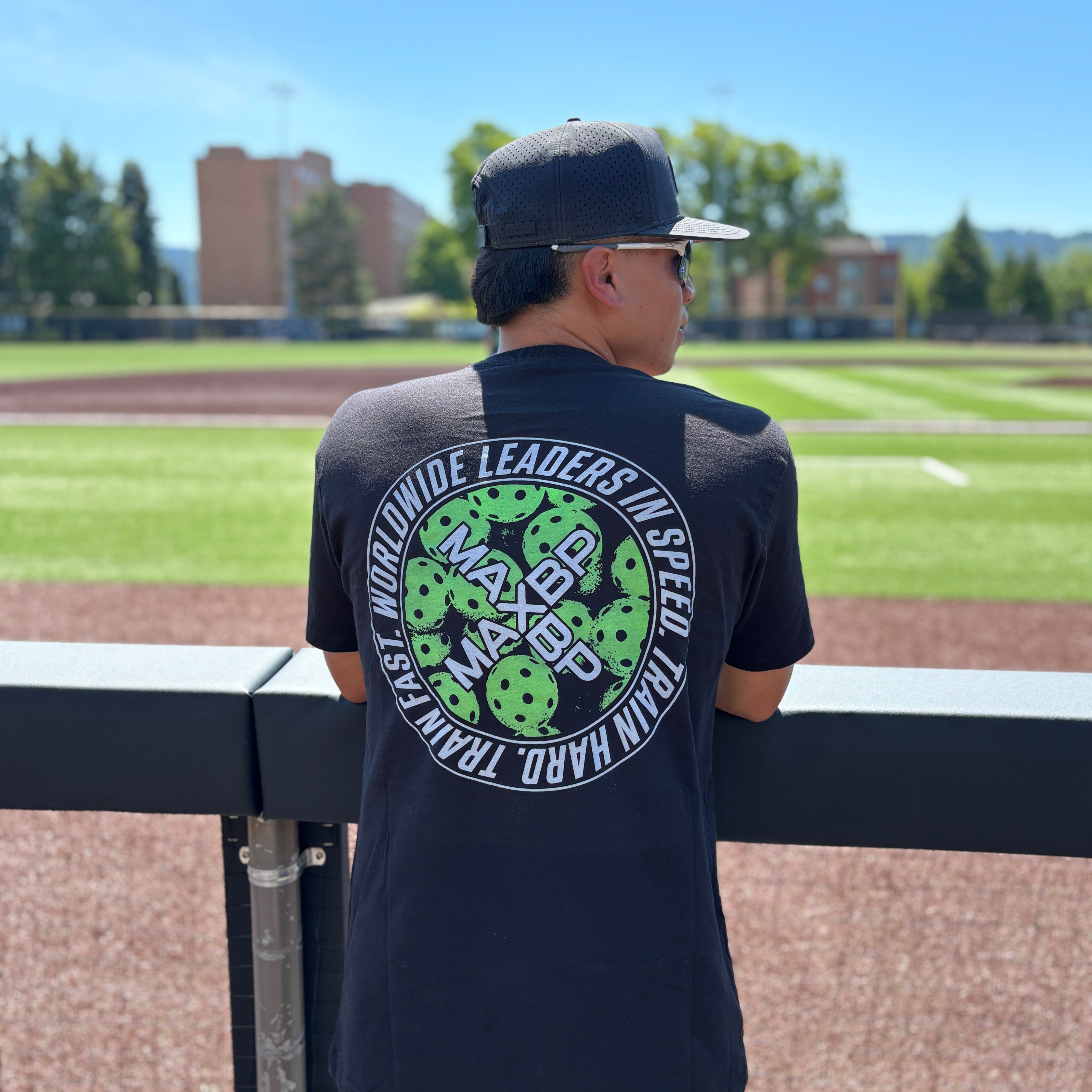 Person wearing a black t-shirt with a logo on a baseball field